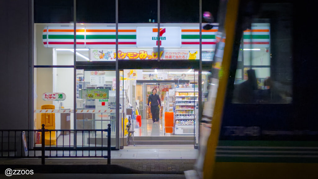 夜の街並み。コンビニの入口と通り過ぎる路面電車