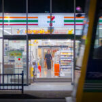 Night street scene with a convenience store entrance and a passing tram
