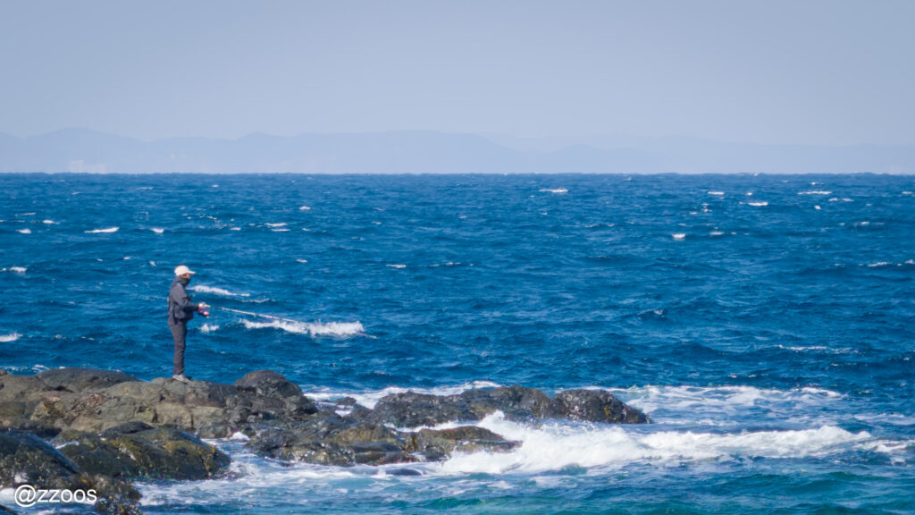 A fisherman fishing on rocks despite the rough waves.